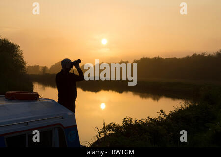 Maison de vacances sur l'homme sur le pont de bateaux de plaisance voile photographier un coucher de soleil sur la rivière ant, les Norfolk Broads, UK, mai. Banque D'Images