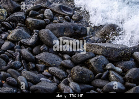 Rochers noirs couvrir la plage à Hilo, Hawaii, comme une vague, submergeant des roches sous sa mousse d'ébullition. Banque D'Images