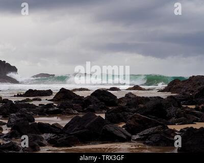 Temps orageux sauvage sur la plage, vagues bleu vert qui roulent, s'écrasent sur les rochers, nuages gris violet, de devant, l'Australie Banque D'Images