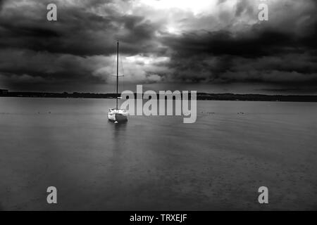 Petit voilier sous un ciel orageux inquiétant flottante comme il commence à pleuvoir. Banque D'Images