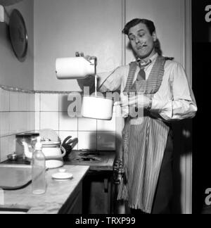 L'homme des années 50. Le danseur Mario Mengarelli suédois dans la cuisine occupé à verser le lait dans une casserole. Un biberon est vu sur le banc et peut être que son petit enfant est en attente d'un repas. La Suède 1952 ref 1958 Banque D'Images