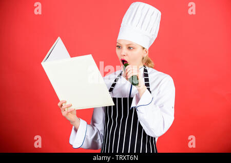 Woman in hat cook et de l'aire de manger le concombre. chef professionnel en cuisine. Cuisine. Femme au foyer avec livre de cuisine. happy woman cooking alimentation saine par recette. menu du restaurant. Suivre un régime culinaire. Banque D'Images