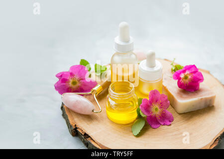Spa huiles essentielles. Spa Nature morte avec bouteille d'huile de rose musquée et de rouleau de quartz, fleurs, spa & Soins de beauté sur planche de bois Banque D'Images