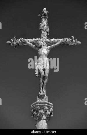 Photo monochrome d'une statue de pierre du Christ sur la croix à un cimetière dans la Feuillée, Bretagne, France. Banque D'Images