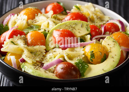 Recette salade de pâtes farfalle avec avocat mûr, les oignons et les tomates en gros plan un bol sur la table horizontale. Banque D'Images