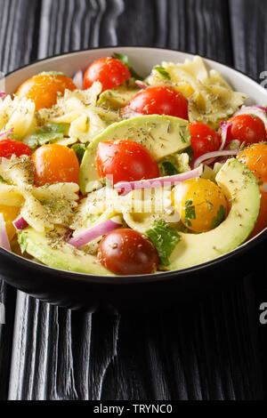 Pâtes Farfalle avec avocat mûr, les oignons et les tomates close-up dans un bol sur la table verticale. Banque D'Images