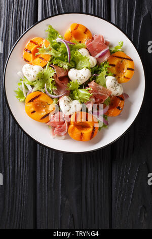 Facile salade diététique avec de la mozzarella, le prosciutto, les abricots grillés, oignons rouges et la laitue sur une assiette sur la table. Haut Vertical Vue de dessus Banque D'Images