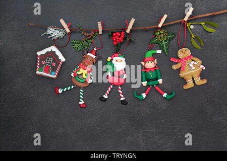 Décorations de Noël suspendu à une branche avec de la flore et de l'hiver noël du père Noël, du renne, Elf, gingerbread house et lady cookie on dark Banque D'Images