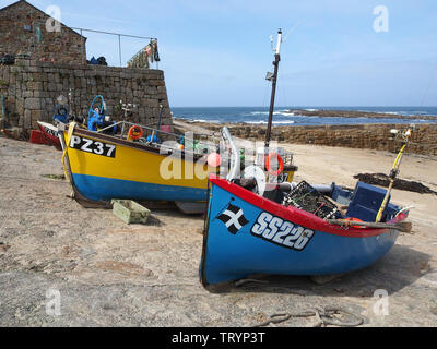 Un groupe de bateaux de pêche très colorés s'est transporté jusqu'au quai de Sennen Cove, en Cornouailles, en Angleterre, avec le ciel bleu et la mer bleue au-delà. Banque D'Images