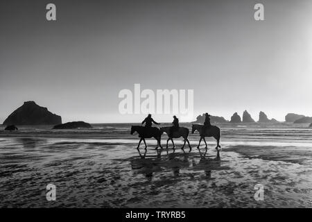 Un groupe de 3 cavaliers apprécier le coucher du soleil sur la plage de Bandon. Banque D'Images