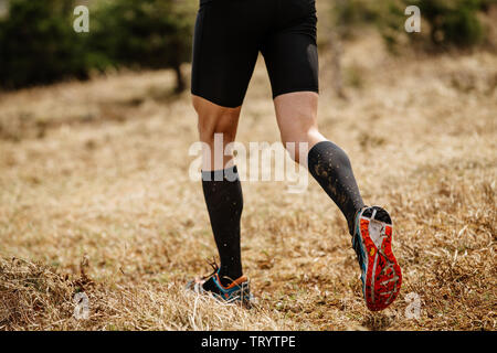 Homme jambes runner en Noir Chaussettes de compression trail run sur herbe sèche Banque D'Images