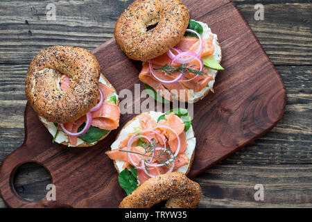 Lox - Tout ce bagel avec du saumon fumé, Épinards, oignons rouges, avocat et fromage à la crème sur une table en bois rustique. Capture d'image en vue de dessus Banque D'Images