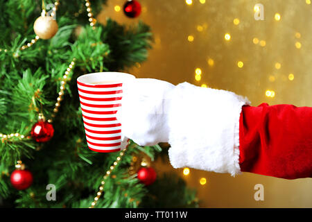 Santa holding mug à la main, sur fond lumineux Banque D'Images