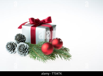 Composition de Noël avec un cadeau enveloppé de ruban rouge, les cônes d'argent, boules rouges et un sapin branch - isolé sur fond blanc Banque D'Images