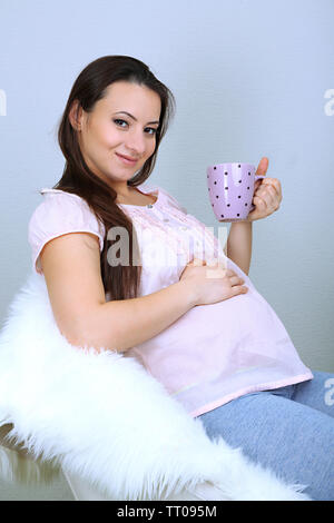 Les jeunes régnant femme assise sur un fauteuil et holding cup sur wall background Banque D'Images