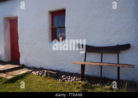 Une vue en gros plan d'un chalet, de la croft porte avant rouge une fenêtre et un banc à l'extérieur contre le mur blanc Banque D'Images