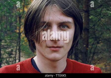 Un beau gars avec de longs cheveux ébouriffés et les yeux verts se dresse au milieu de la forêt d'automne Banque D'Images