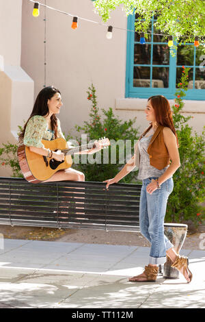 Heureux, souriant, les jeunes femmes hispaniques les amis de s'amuser ensemble en plein air dans un parc de la ville. Une femme joue de la guitare. Banque D'Images