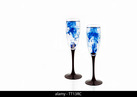 Deux verres à vin sur fond blanc avec des peintures de couleur bleue à l'intérieur. Fougères pour champagne avec de la fumée et les ensemencer. Banque D'Images