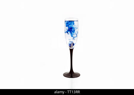 Verre de vin sur fond blanc avec des peintures de couleur bleue à l'intérieur. Fougere pour champagne avec de la fumée et les ensemencer. Banque D'Images