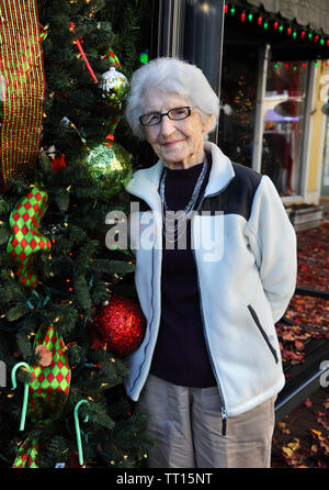 Grand-mère, avec des cheveux blancs et des lunettes, se distingue en plus d'une décoration de Noël tout en faisant du shopping de la rue au centre-ville d'El Dorado, Arkansas. Elle a sur tan Banque D'Images