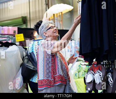 Une femme plus âgée avec des cheveux gris et des lunettes regarde comme elle atteint pour quelque chose alors que le shopping. Pays Colporteur Show Robstown, Texas USA. Banque D'Images