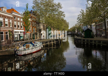 Gouda, Hollande, Pays-Bas, Avril 23, 2019, vélos et stationné près d'un pont le long d'une rue, canal à Gouda vieille ville. Parterres de fleurs dans un bateau, Banque D'Images