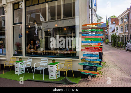 Gouda, Hollande, Pays-Bas, le 23 avril 2019. Vieille ville de Gouda, café et une fenêtre de nombreux panneaux de direction de couleur sur un poteau de la rue des façades de style hollandais Banque D'Images