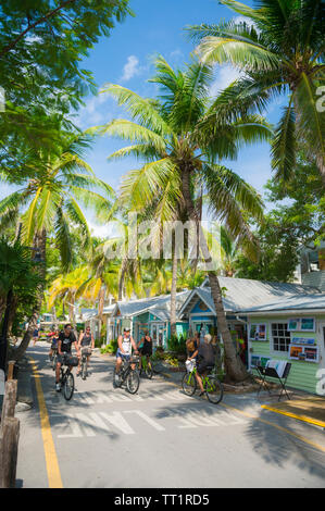 KEY WEST, Floride, USA - Septembre 2018 : les visiteurs de la bicyclette le long d'une rue bordée de maisons aux couleurs vives convertis en magasins dans la vieille ville. Banque D'Images