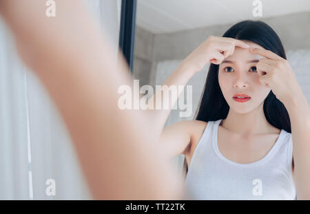 Young Asian woman squeeze face au problème d'acné à miroir. Banque D'Images