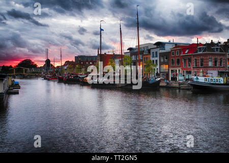 Canal avec de vieux navires un moulin à vent et un pont-levis au coucher du soleil, Leiden, Pays-Bas Banque D'Images
