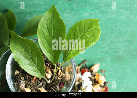 Tasse en verre avec des fleurs et d'herbes sèches, de fruits Ingrédients pour le thé, sur la couleur de fond de bois Banque D'Images