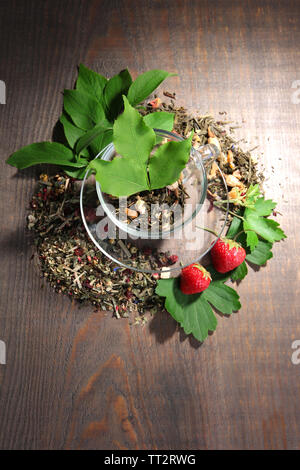 Tasse en verre avec des fleurs et d'herbes sèches, de fruits Ingrédients pour le thé, sur la couleur de fond de bois Banque D'Images