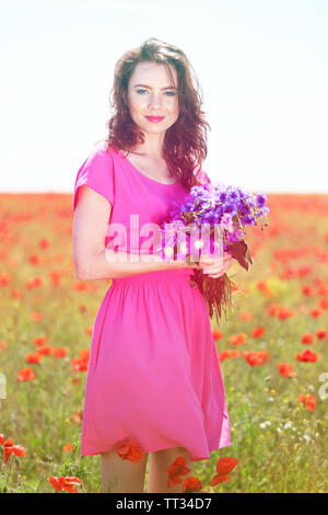 Belle jeune femme avec des fleurs dans champ de coquelicots Banque D'Images