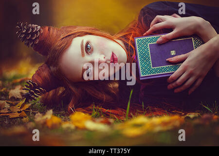 Portrait d'une belle jeune fille rousse avec une coiffure inhabituelle avec un livre dans l'automne forêt féerique. Un fabuleux automne photo shoot. Saison d'automne. C Banque D'Images