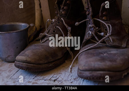 Vintage ancien usé bottes de travail et une tasse Banque D'Images