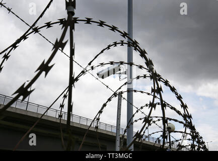 Close-up de barbelés et de barbelés surounding une enceinte protégée dans l'Est de Londres, Royaume-Uni. Montre caméra de sécurité et l'éclairage. Au-delà de la route viduct. Banque D'Images