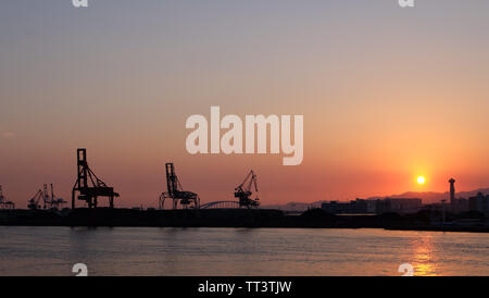 Osaka, Japon - 24 mai 2019 : Silhouette de grues de chargement port en face d'une baie, près de Port d'Osaka, avec le coucher de soleil et crépuscule dans le ciel. Banque D'Images