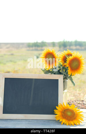 Beaux tournesols dans un vase et cadre vide sur la table en bois sur fond de champ Banque D'Images