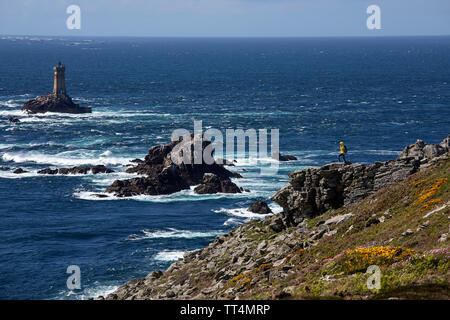 Dans yellow jacket femme debout sur le terrain rocheux à la Pointe du Raz, l'un des monuments les plus spectaculaires de Bretagne, et le phare de la Vieille, Franc Banque D'Images