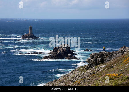 Dans yellow jacket femme debout sur le terrain rocheux à la Pointe du Raz, l'un des monuments les plus spectaculaires de Bretagne, et le phare de la Vieille, Franc Banque D'Images