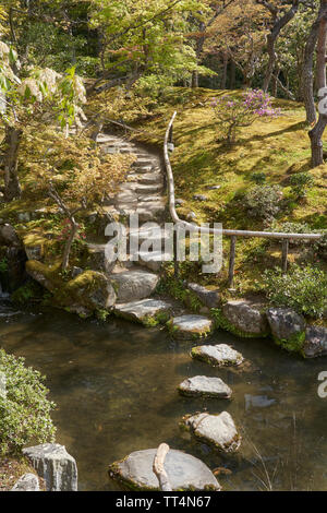 Jardin japonais avec un sentier en pierre de l'autre côté de la rivière. Le chemin continue ensuite jusqu'à la colline. Banque D'Images