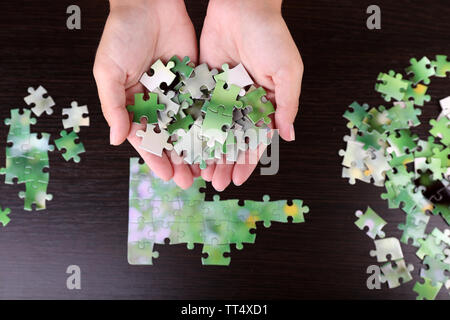 Pièce du puzzle dans les mains sur fond de table en bois Banque D'Images