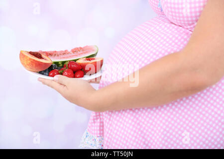 Young pregnant woman holding plate avec des fruits sur fond lumineux Banque D'Images