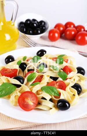 Spaghetti aux tomates, olives, huile d'olive et les feuilles de basilic sur plaque sur fond de tissu Banque D'Images