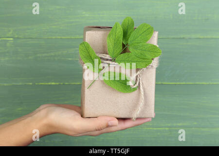 Tenir la main femme style naturel boîte cadeau artisanal avec des feuilles fraîches et ficelle rustique, sur fond de bois Banque D'Images