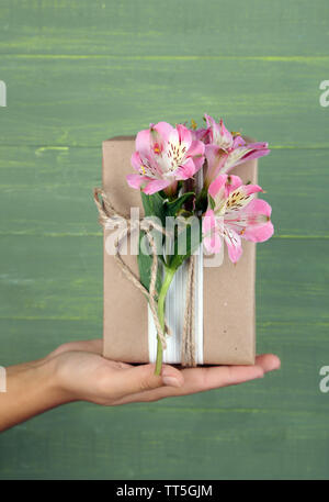 Tenir la main femme style naturel boîte cadeau fait à la main avec des fleurs fraîches et ficelle rustique, sur fond de bois Banque D'Images