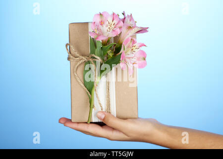 Tenir la main femme style naturel boîte cadeau fait à la main avec des fleurs fraîches et ficelle rustique, sur un fond de couleur Banque D'Images