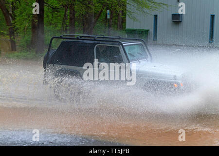 Une voiture de manière explosive par les éclaboussures d'eau dangereusement élevé sur une route inondée de la rivière Banque D'Images