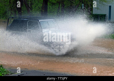 Une voiture de manière explosive par les éclaboussures d'eau dangereusement élevé sur une route inondée de la rivière Banque D'Images